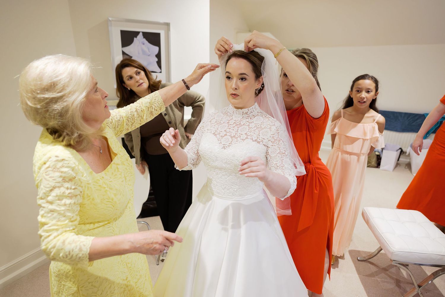 Bridesmaids in colorful dresses helping with wedding preparations in a white room.