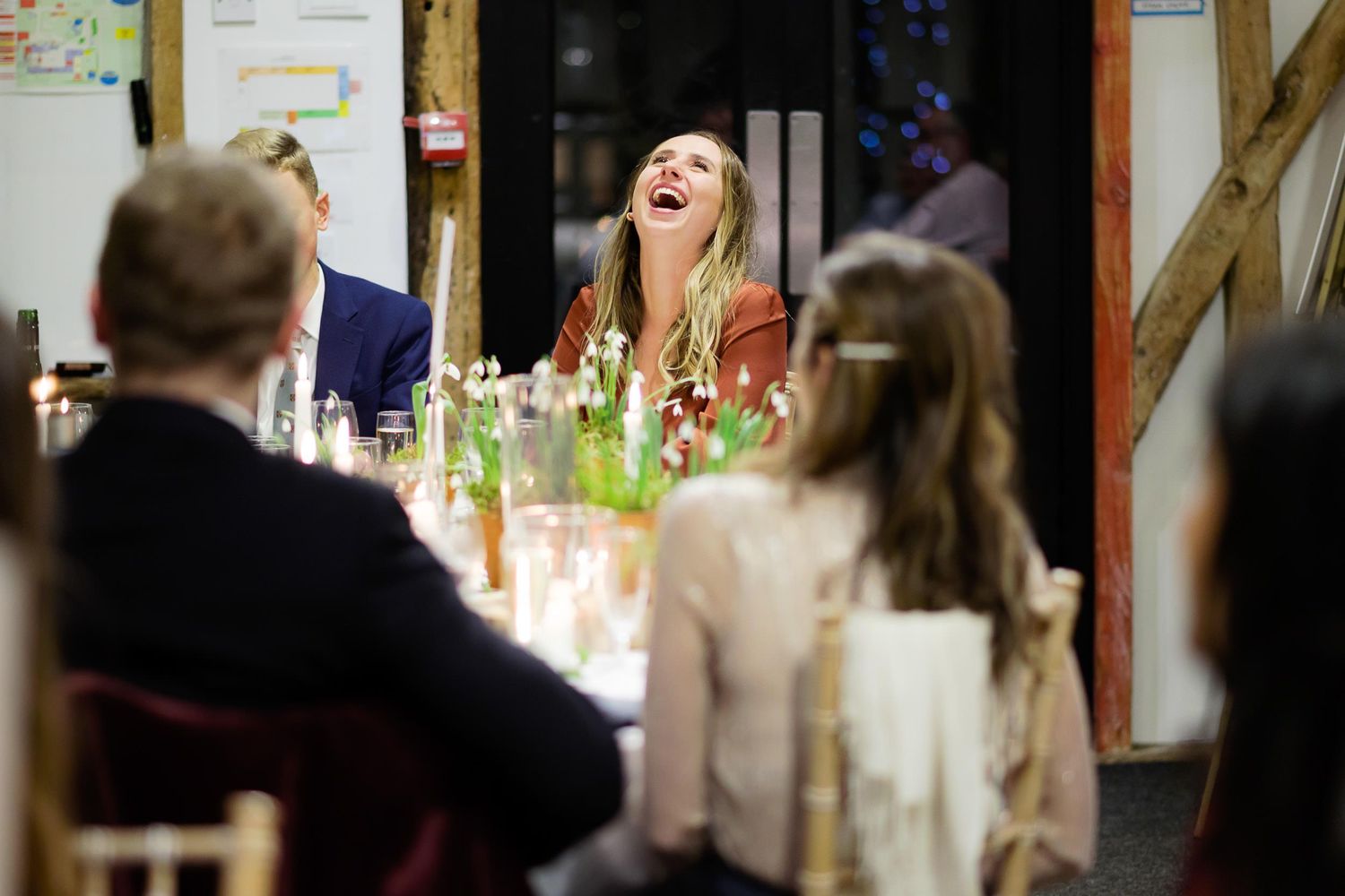 Guest laughing joyfully at wedding reception dinner surrounded by candles and decor.