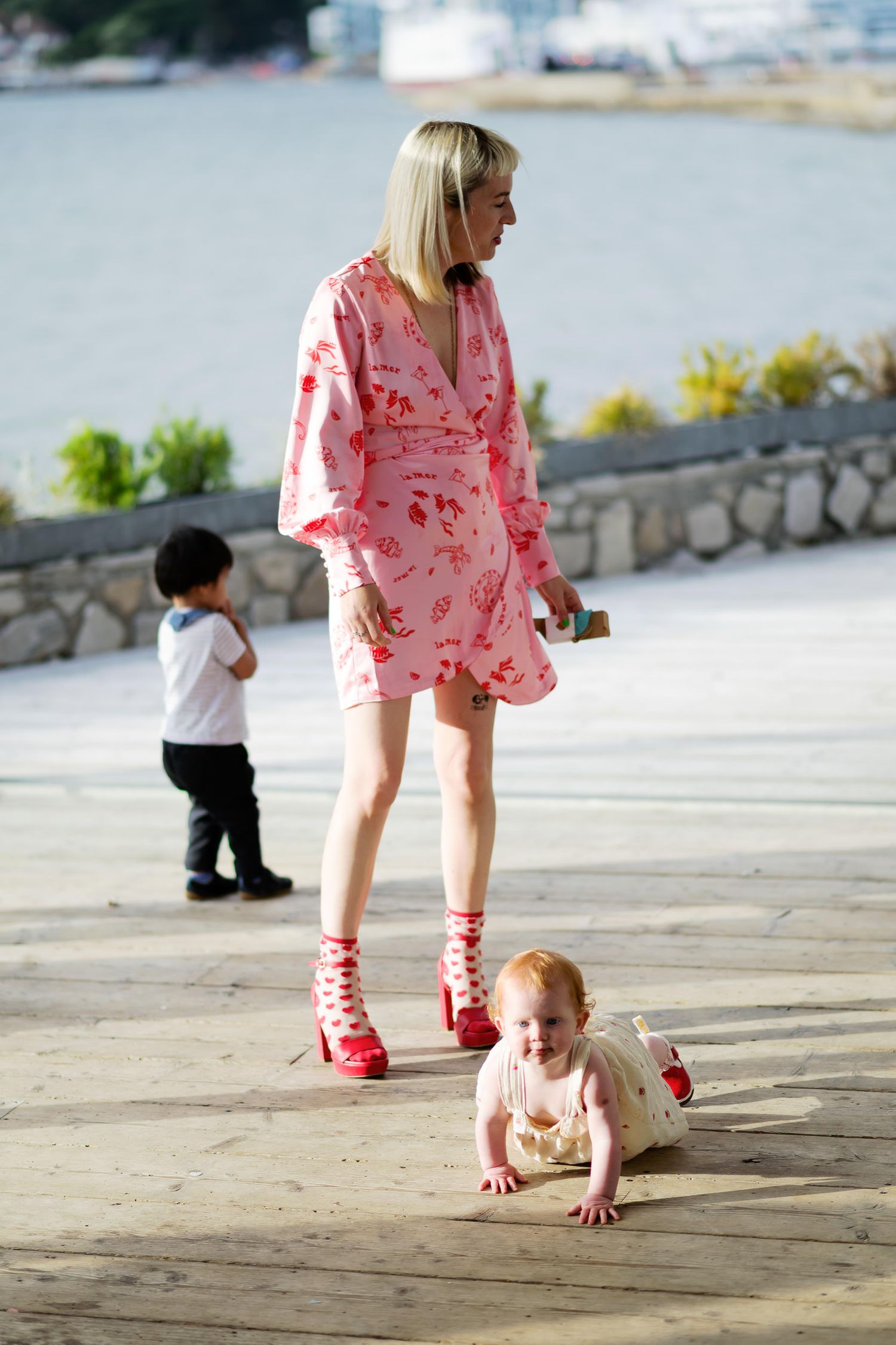 Pink floral dress and matching lace-up shoes on boardwalk with children playing by the water.