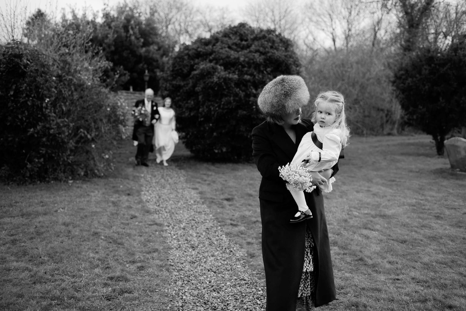 Black and white outdoor portrait of guest holding child at wedding celebration.