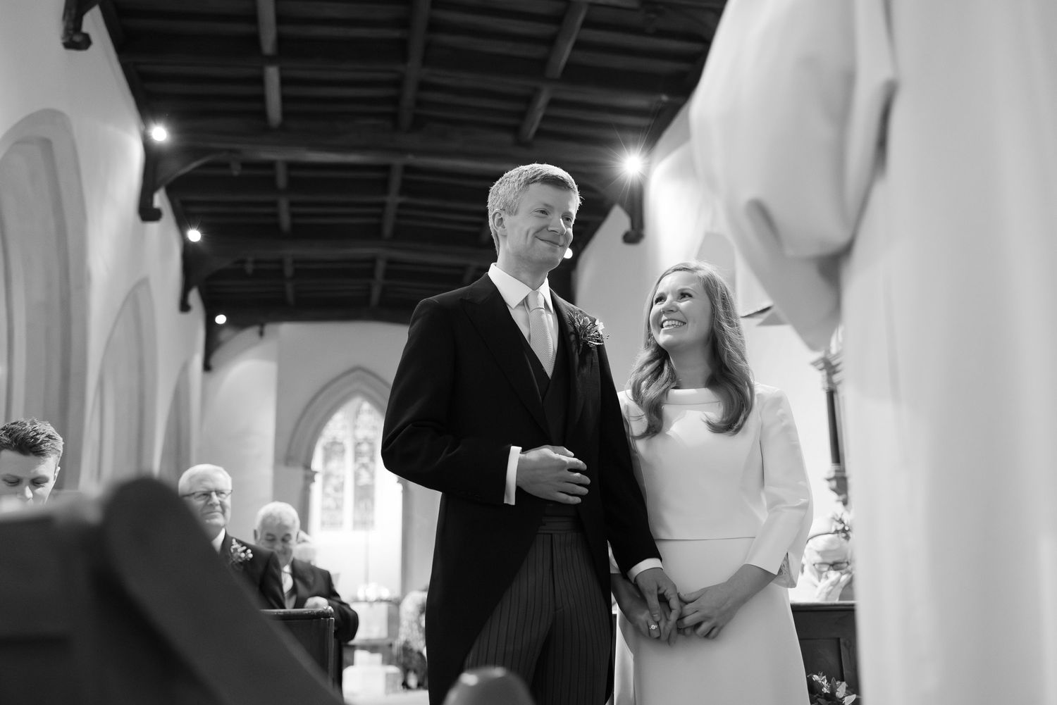 Wedding ceremony guests gathered in a church with elegant white decor and natural lighting.