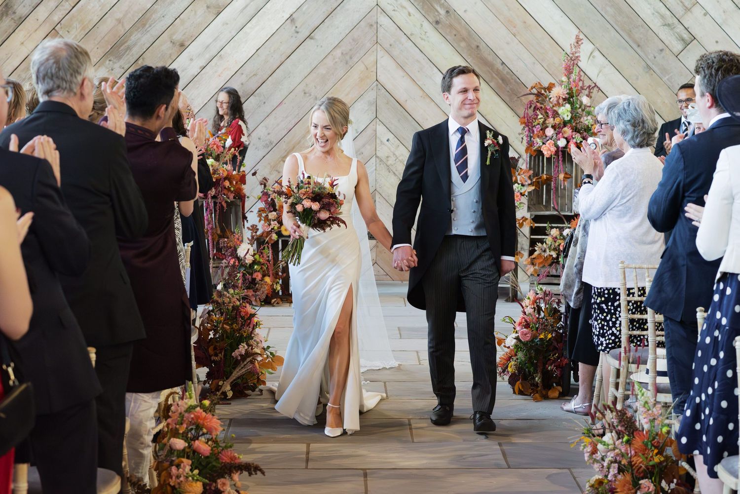 Wedding ceremony space with geometric wooden wall backdrop and floral decorations.