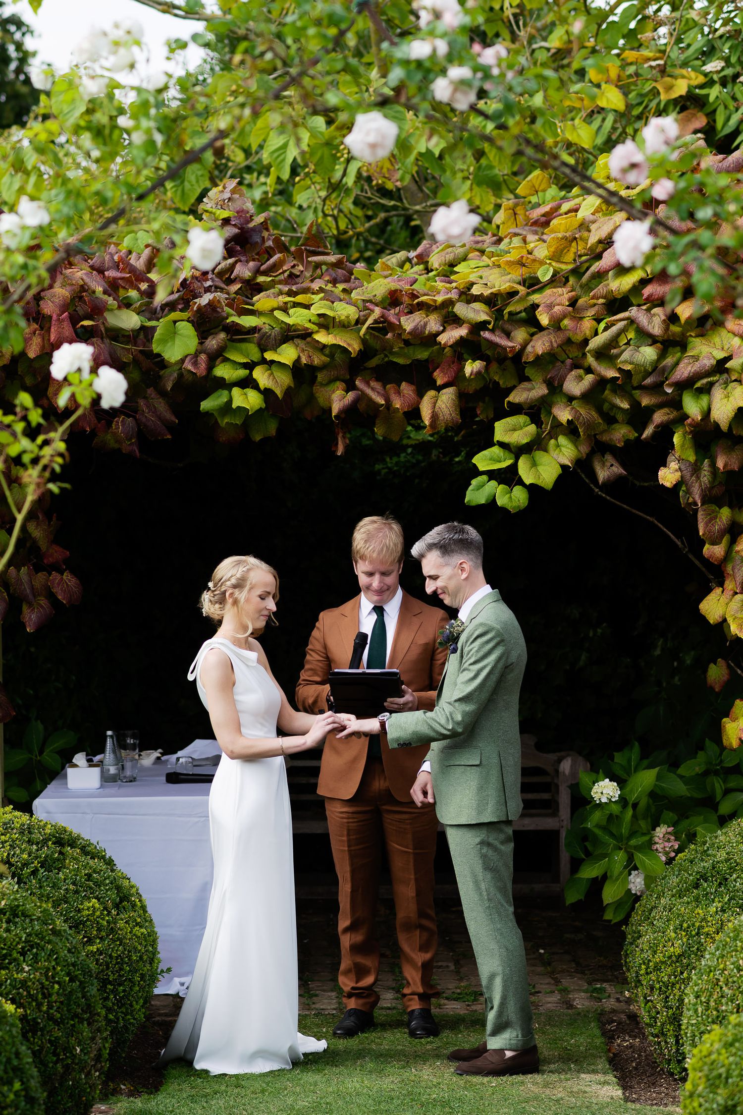 Wedding ceremony taking place under floral arch with officiant and couple in elegant attire.