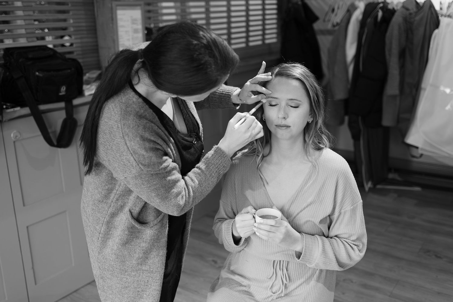 Wedding party members getting makeup and hair done during bridal preparations in black and white.