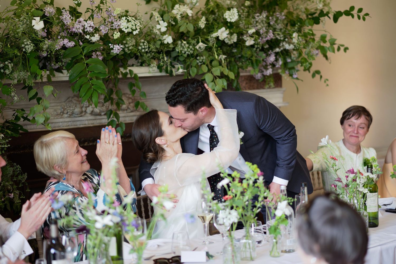 Bride and Groom having a kiss during their wedding speeches surrounded by a floral display at Gunnersbury Park House in London