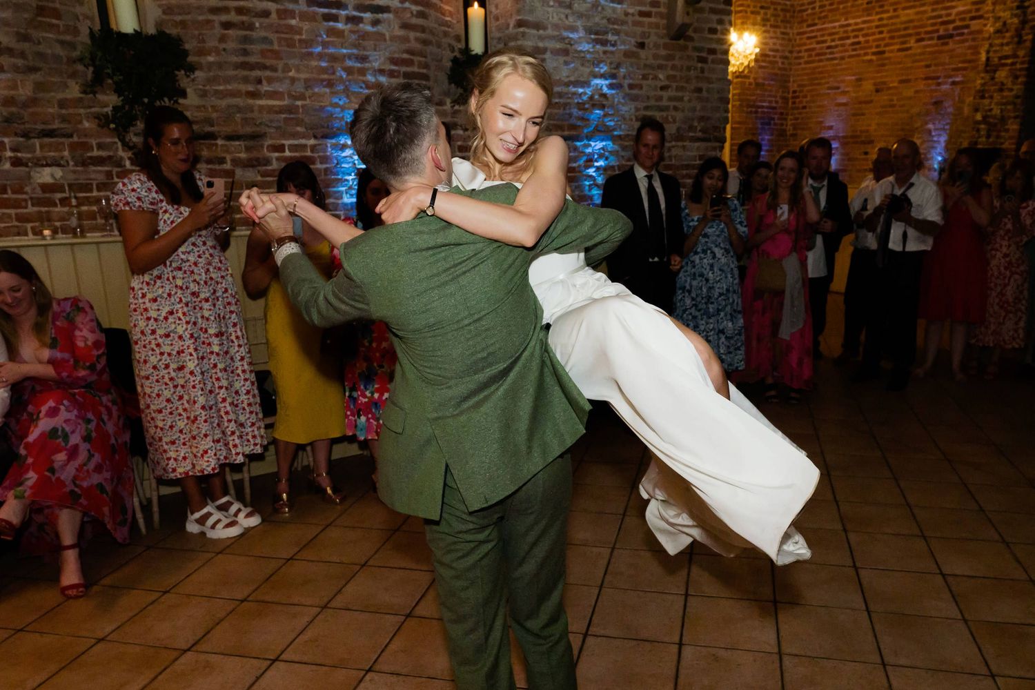 Guests perform spirited dance moves during a wedding reception in a rustic brick venue.