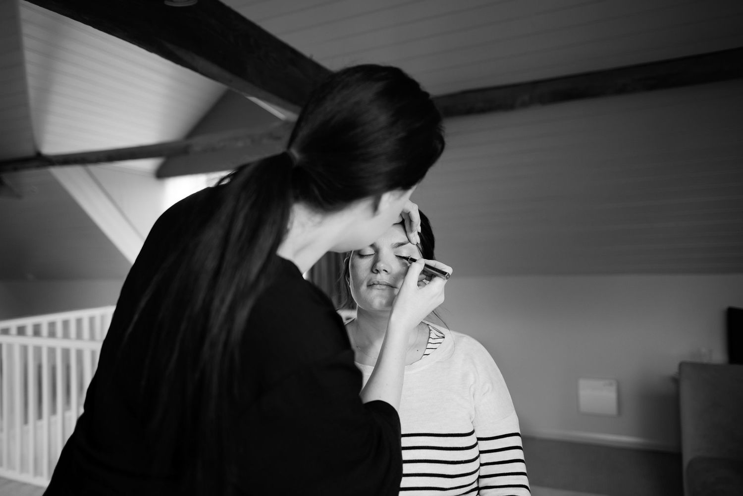 Makeup artist carefully applying cosmetics in an intimate black and white portrait.