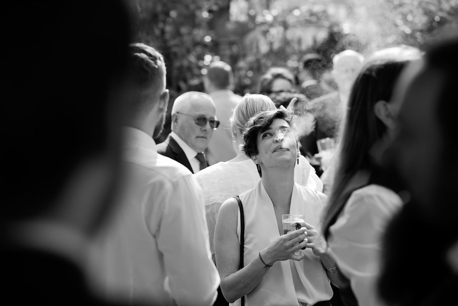A black and white photograph shows a crowd gathering outdoors with figures standing close together.