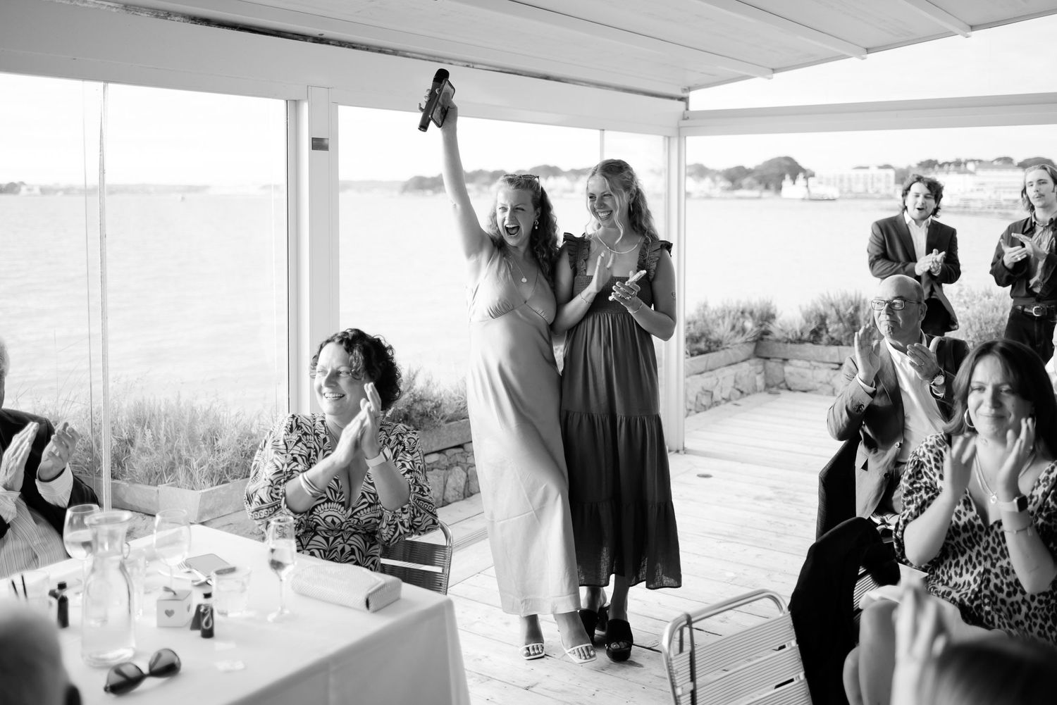 Guests celebrating at a waterfront party with raised arms and joyful expressions.