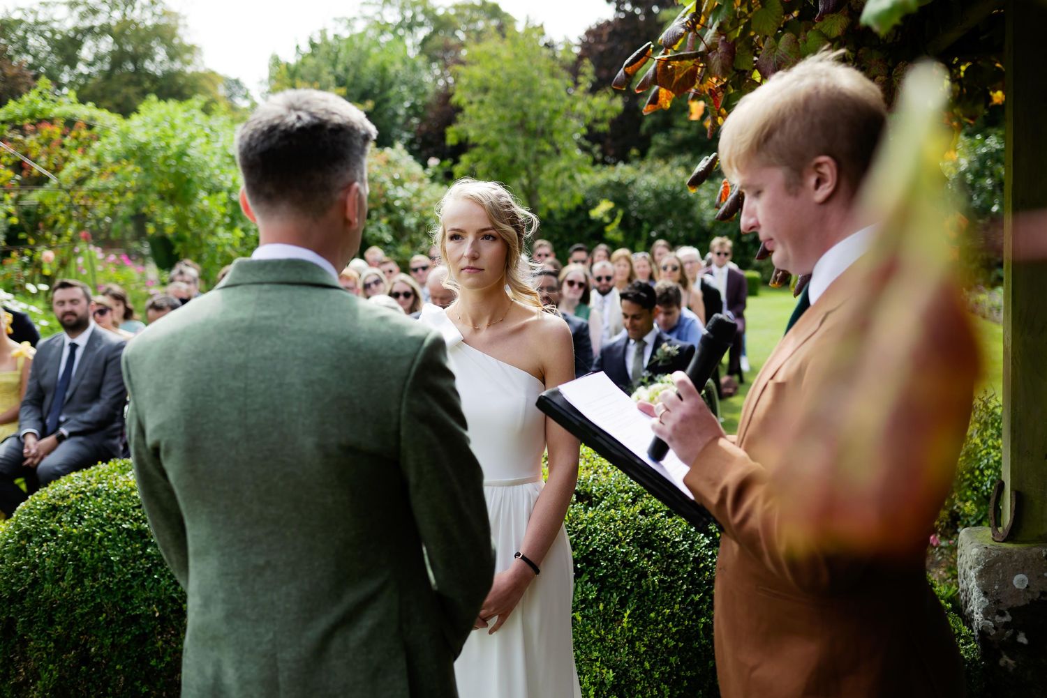 An outdoor garden wedding ceremony with guests gathered around during the vow exchange.