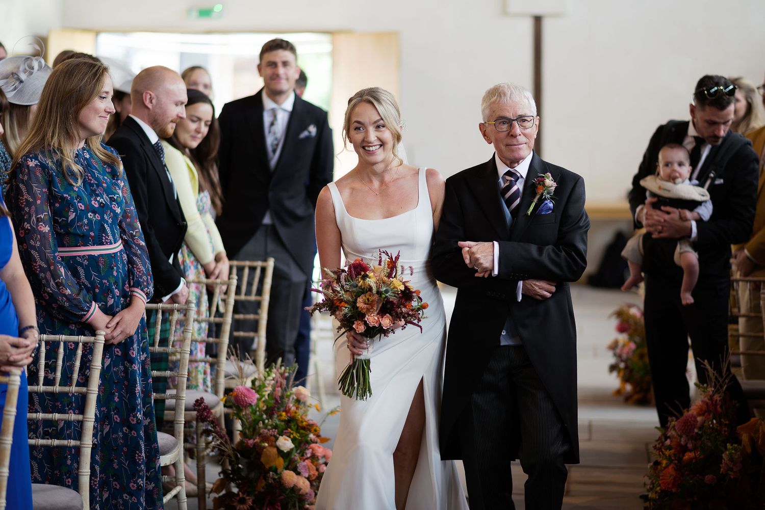 Wedding ceremony setup with floral decorations and guests seated in white chairs.