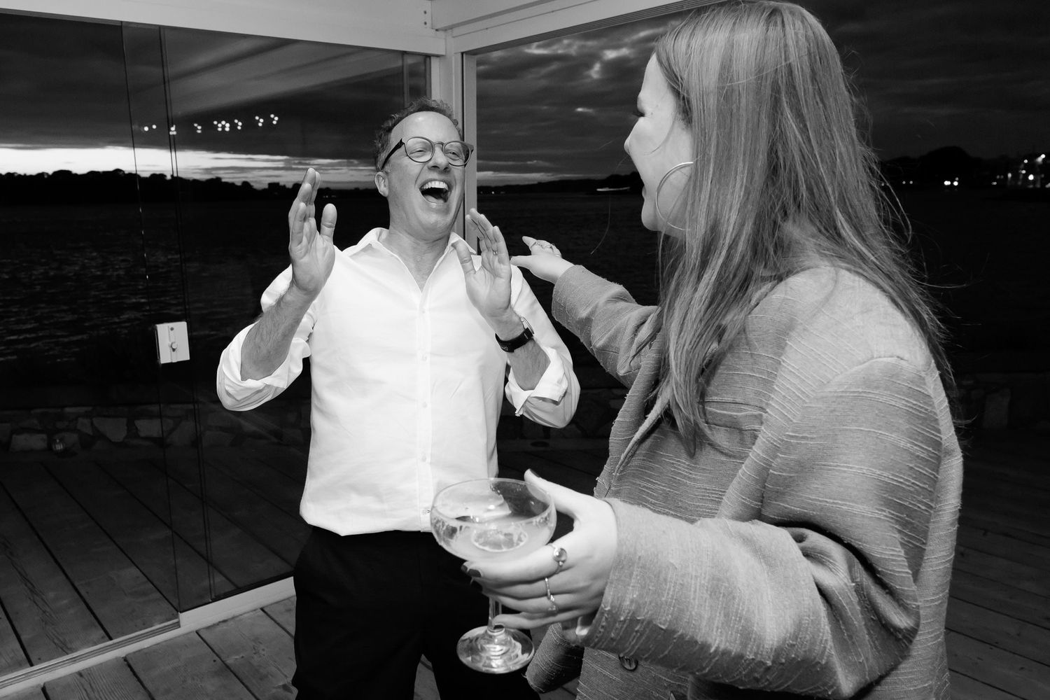 Black and white photo of animated conversation during evening outdoor gathering.