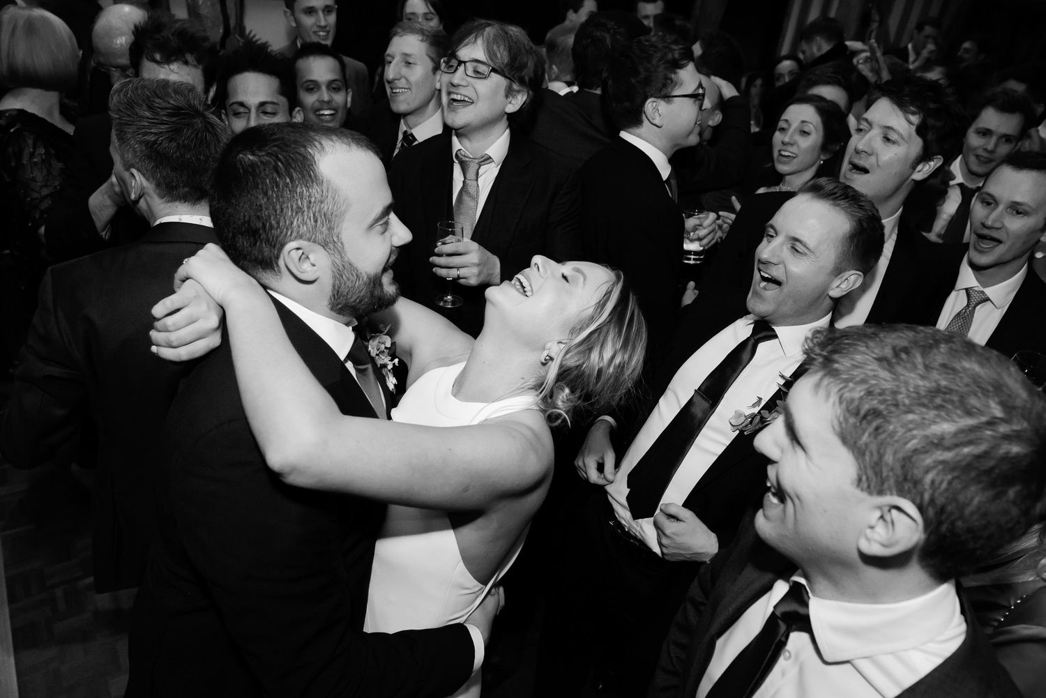 Black and white photo of joyful dancing and celebration at an indoor wedding reception.