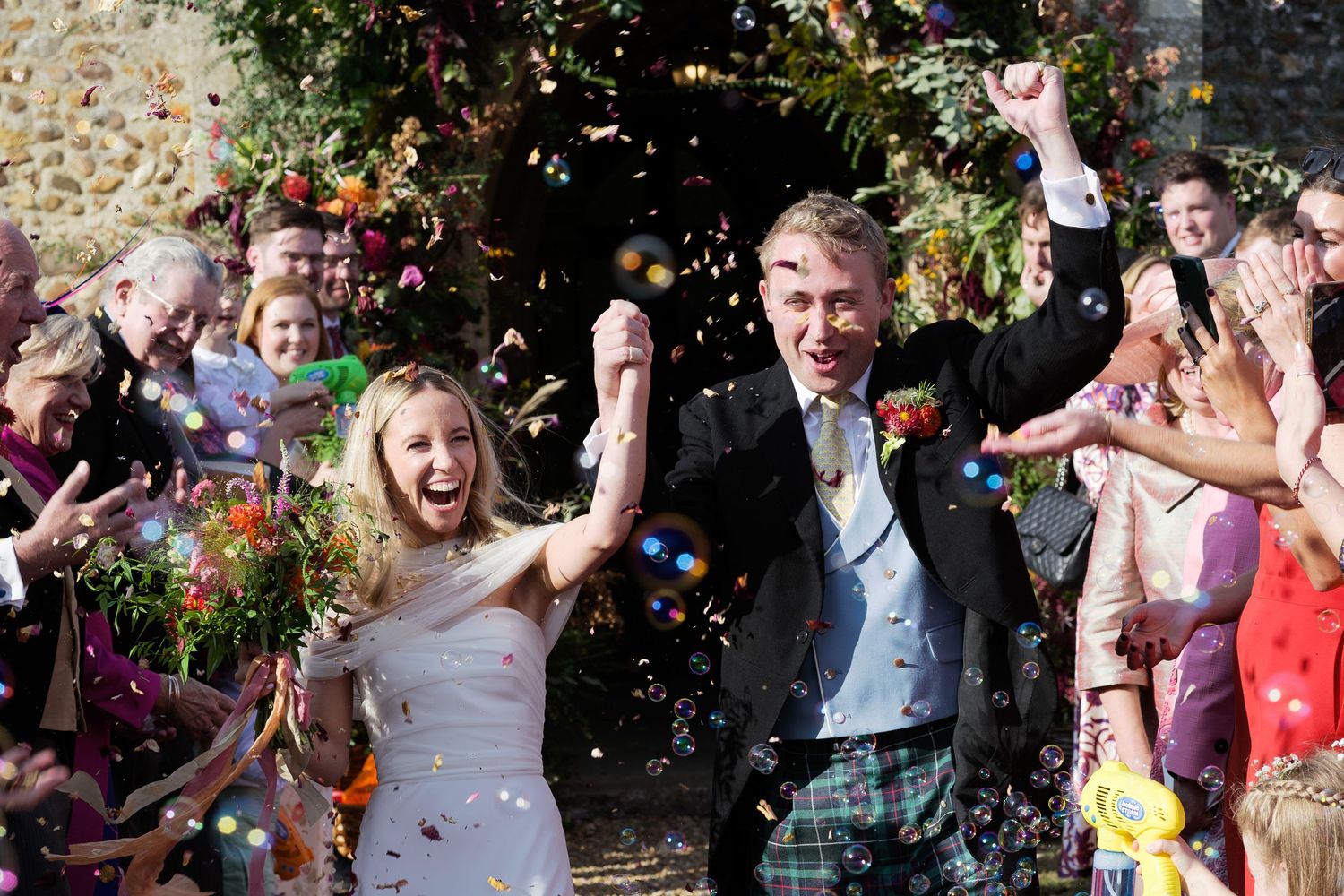 Joyful wedding celebration with confetti being thrown in an outdoor garden setting.