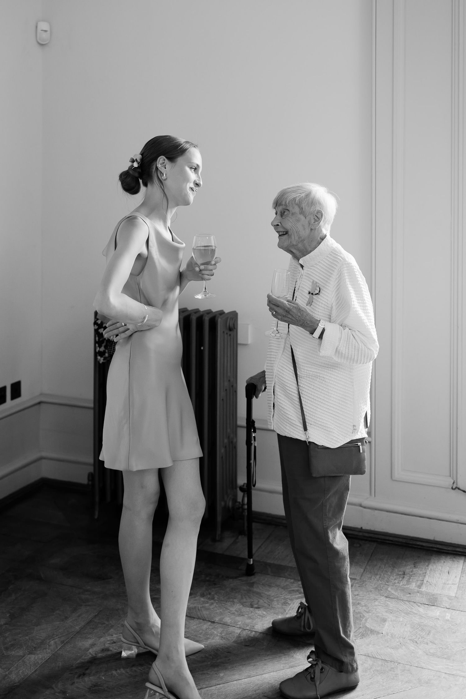 Black and white photo of two people sharing drinks and conversation by a window.