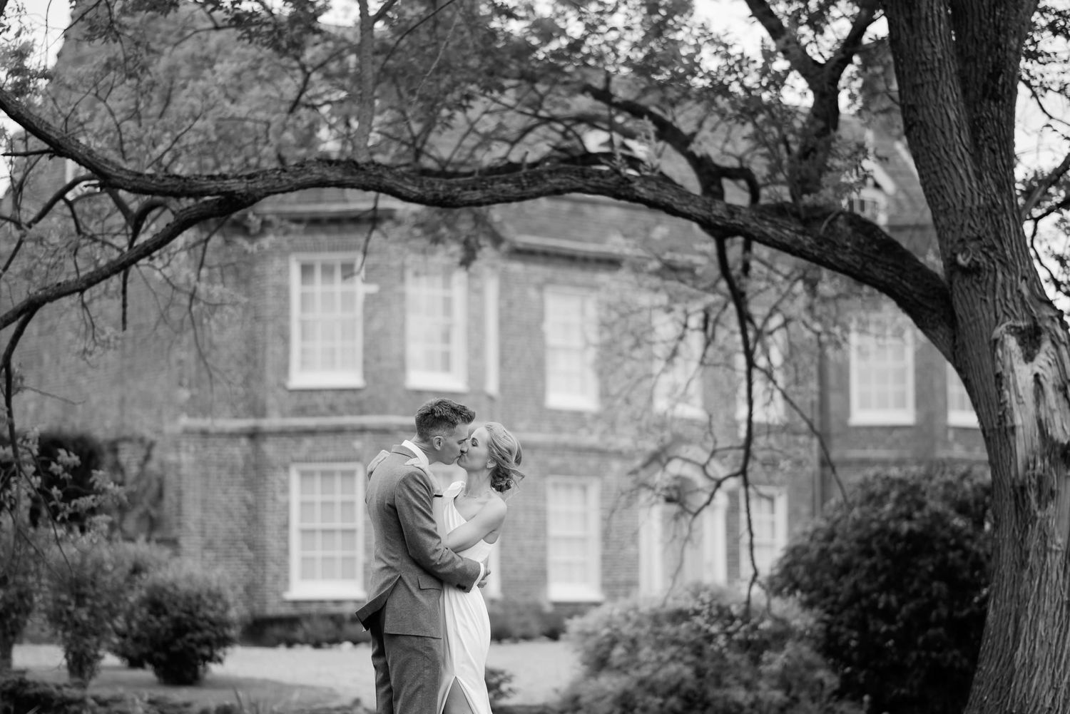 A romantic black and white wedding moment captured in an elegant garden setting with a historic mansion in the background.