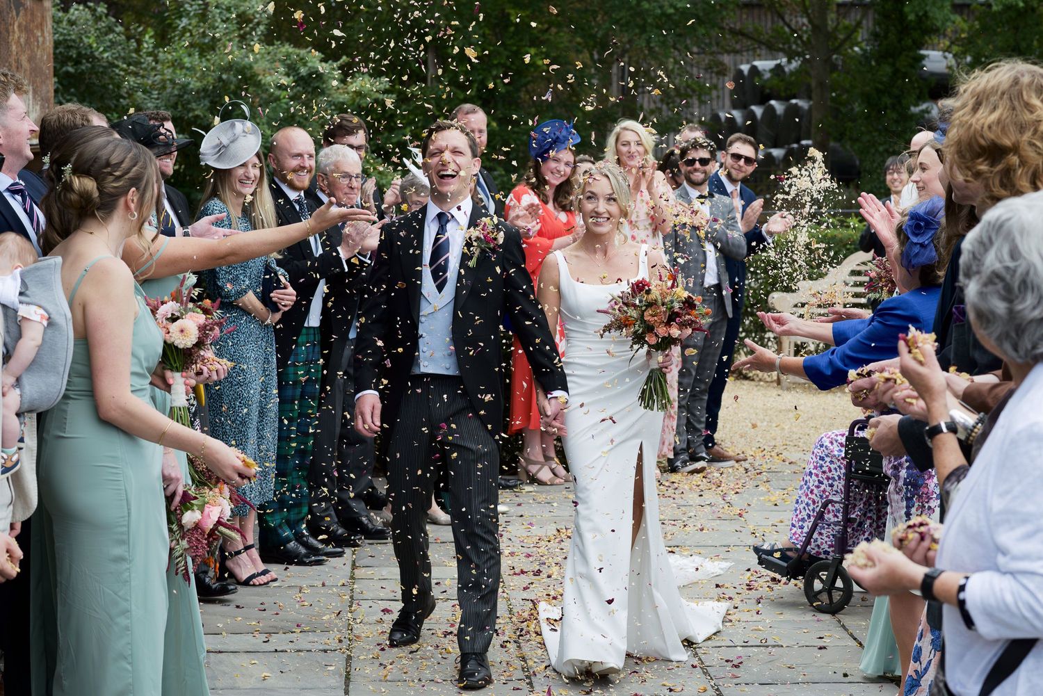 Wedding guests celebrate by throwing confetti at the newlyweds outside during an outdoor ceremony.