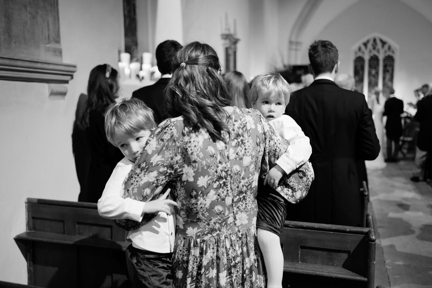 Black and white candid photo of guests embracing children during church wedding ceremony.