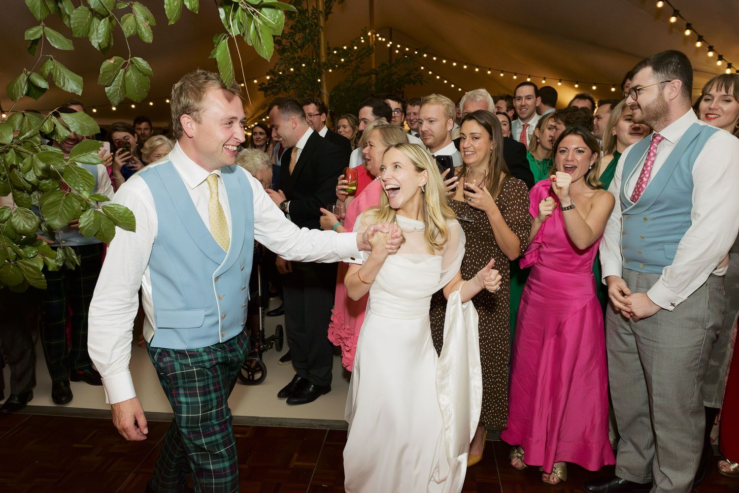 Wedding guests dance and celebrate on the dance floor at a reception decorated with twinkling lights.