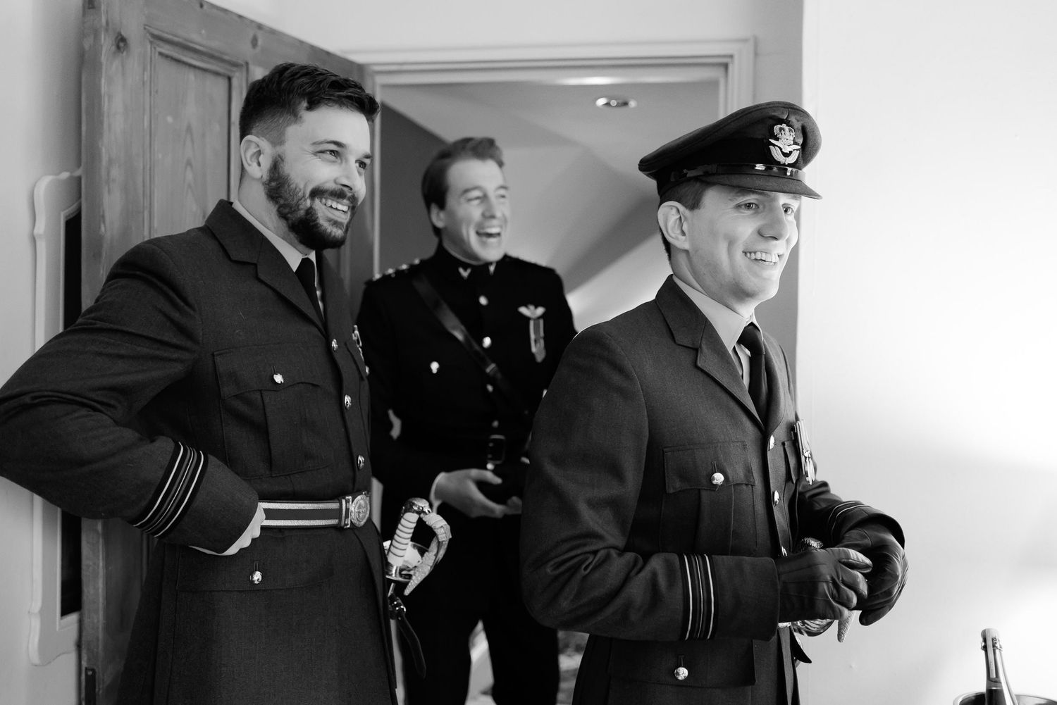 Three uniformed officers in formal military attire share a light moment in a bright hallway.