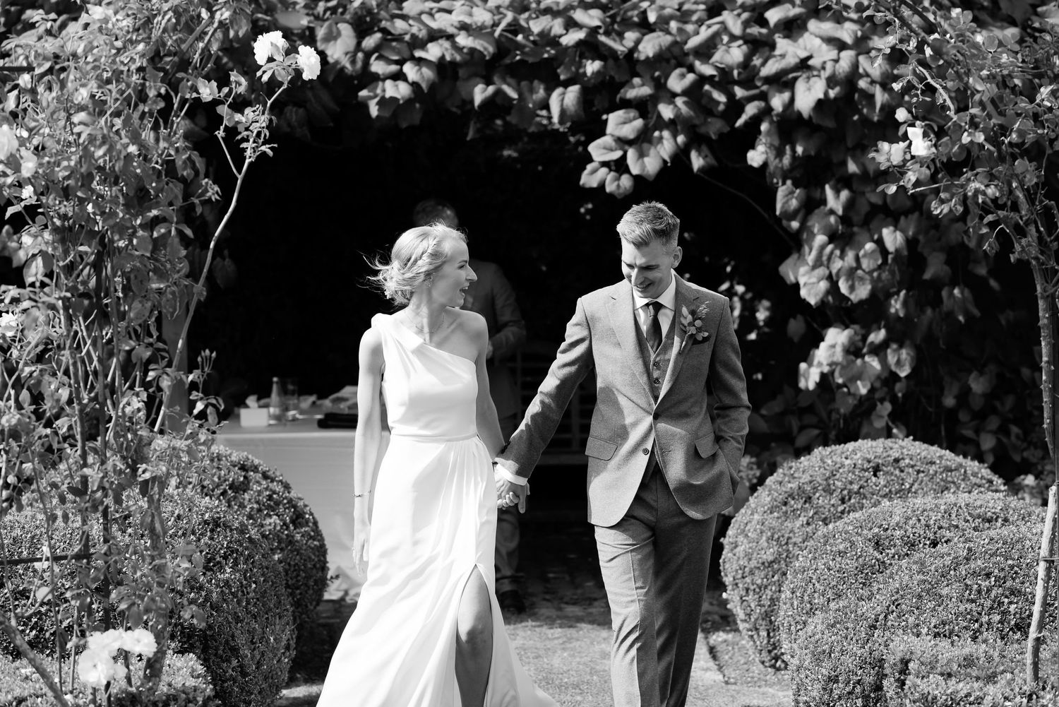 Couple walking together through a garden archway decorated with flowers in black and white.