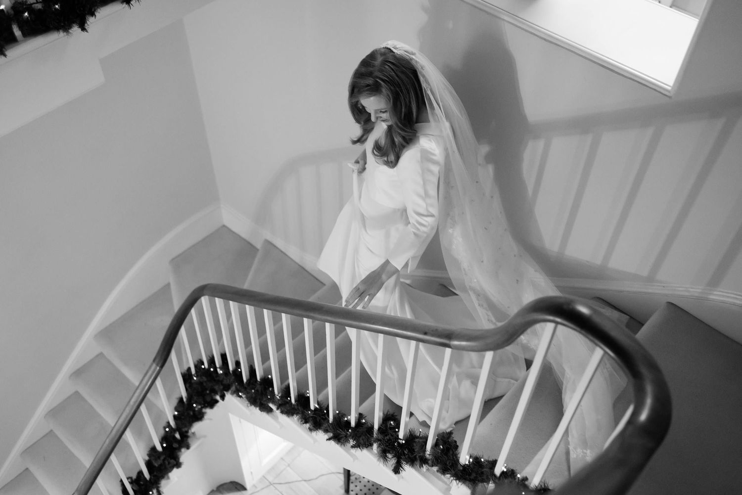 Bride in white gown descending elegant spiral staircase in dramatic lighting.