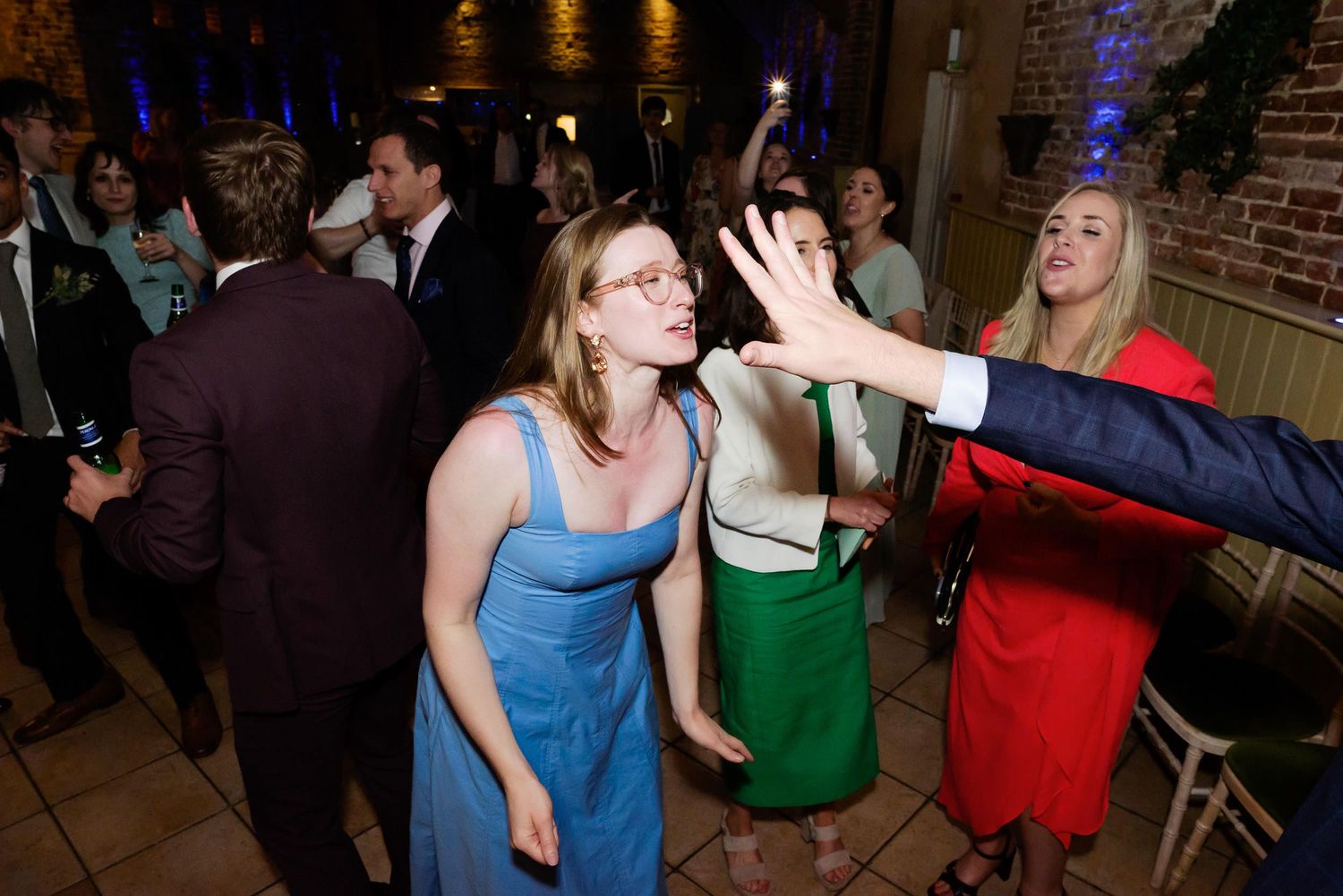 Party guests dance enthusiastically at a reception in a brick-walled venue with ambient lighting.