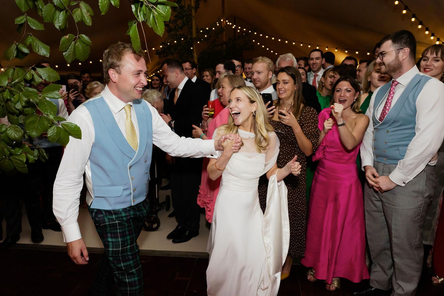 A couple shares a joyful dance moment during a wedding reception as guests smile and watch from the sidelines.