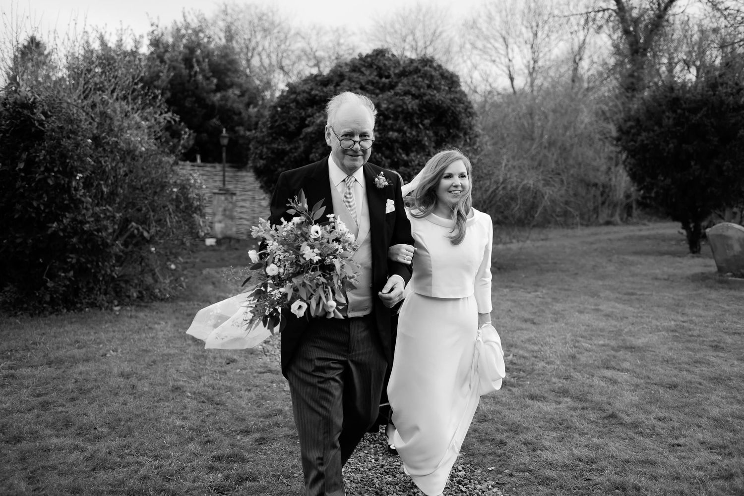 Newlyweds walking together outdoors with bride holding floral bouquet.