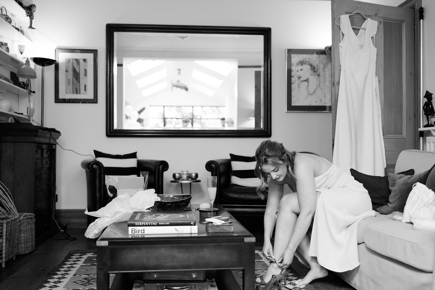 Wedding dress hanging on display while preparations take place in a living room.