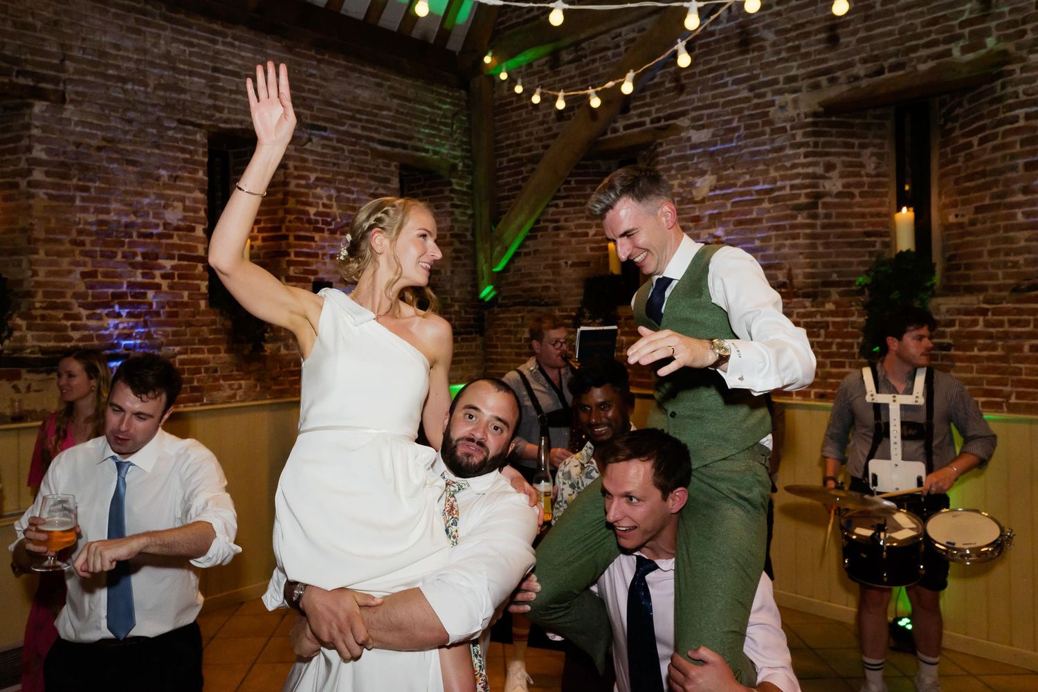Wedding celebration with guests dancing and partying in front of exposed brick walls and string lights.