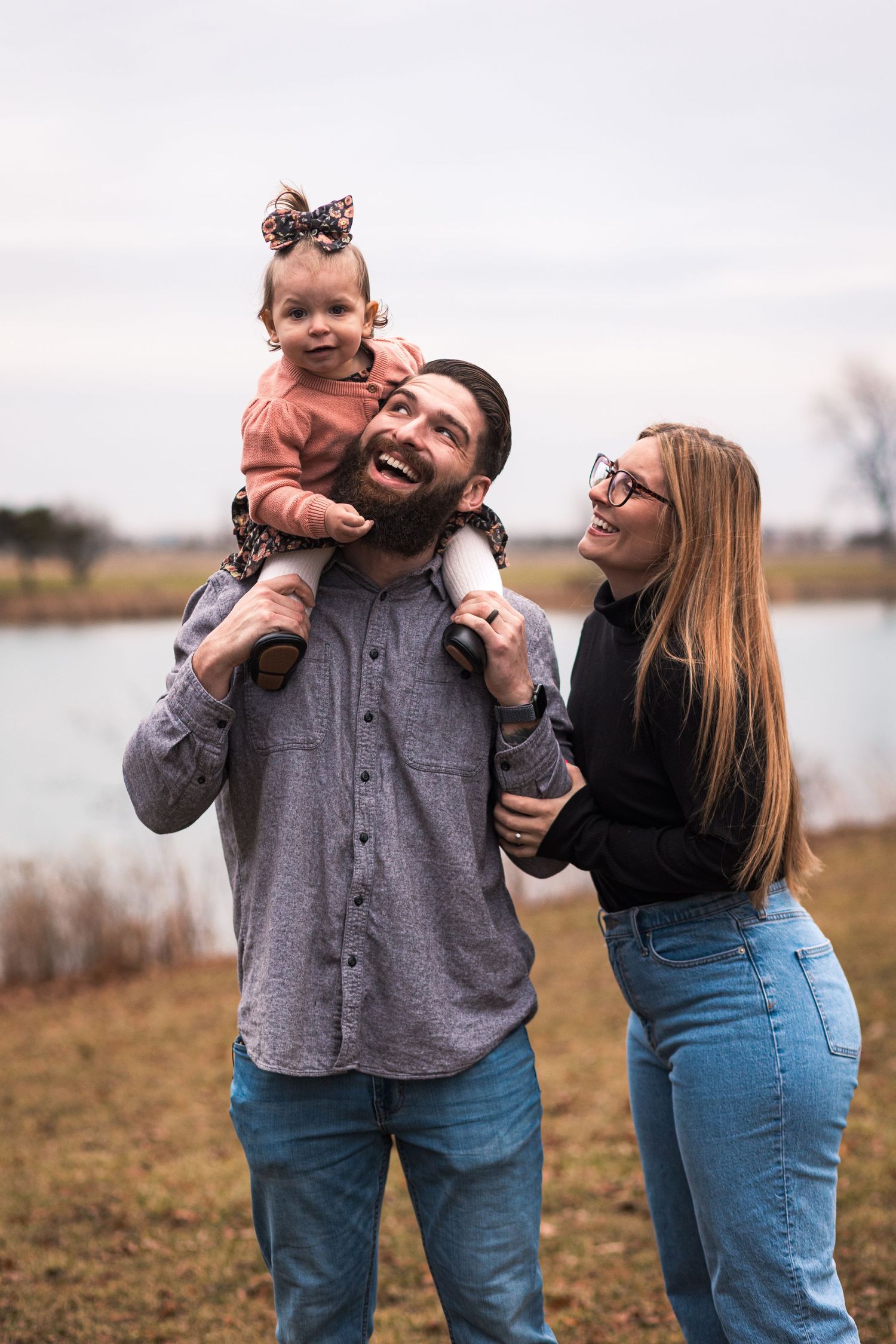 Family session at a lake, showing a family of three smiling together and laughing. JDalbey Photography — family portraits in Champaign, IL.