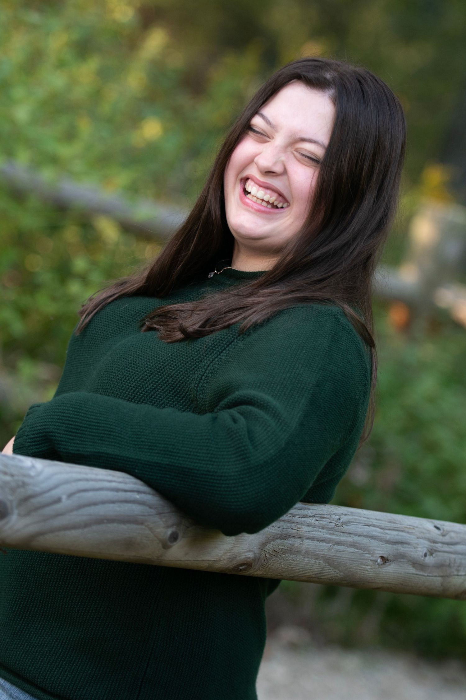 A joyful moment captured outdoors as someone in a dark green sweater leans against a wooden railing with a genuine laugh.