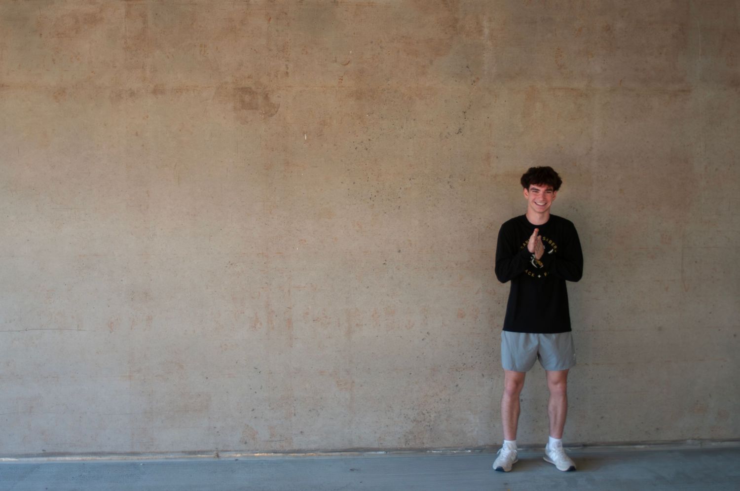 A Franklin high school senior in a black sweatshirt and gray shorts stands excitedly against a beige wall, photographed in profile.