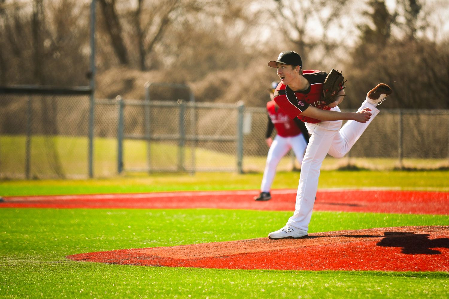 Baseball players practicing pitching mechanics on a field with red dirt infield.