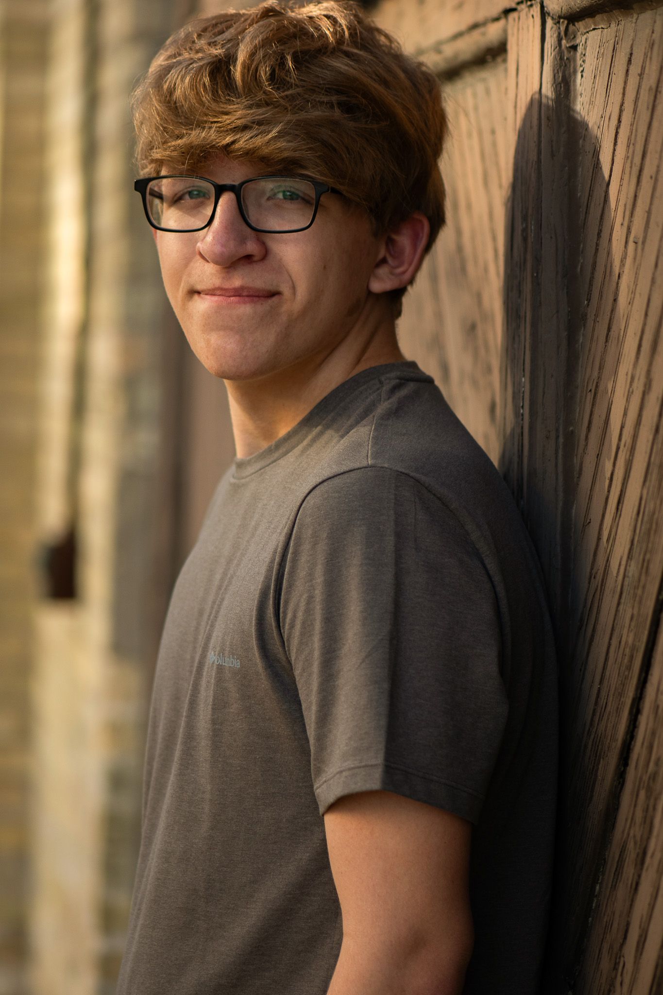 A casual portrait leaning against wooden paneling in warm sunset lighting for his senior portrait session.