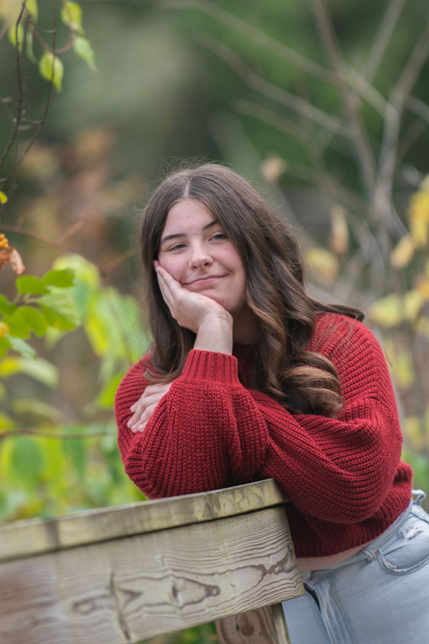 Autumn outdoor portrait featuring someone in a cozy red sweater resting on wooden railing.