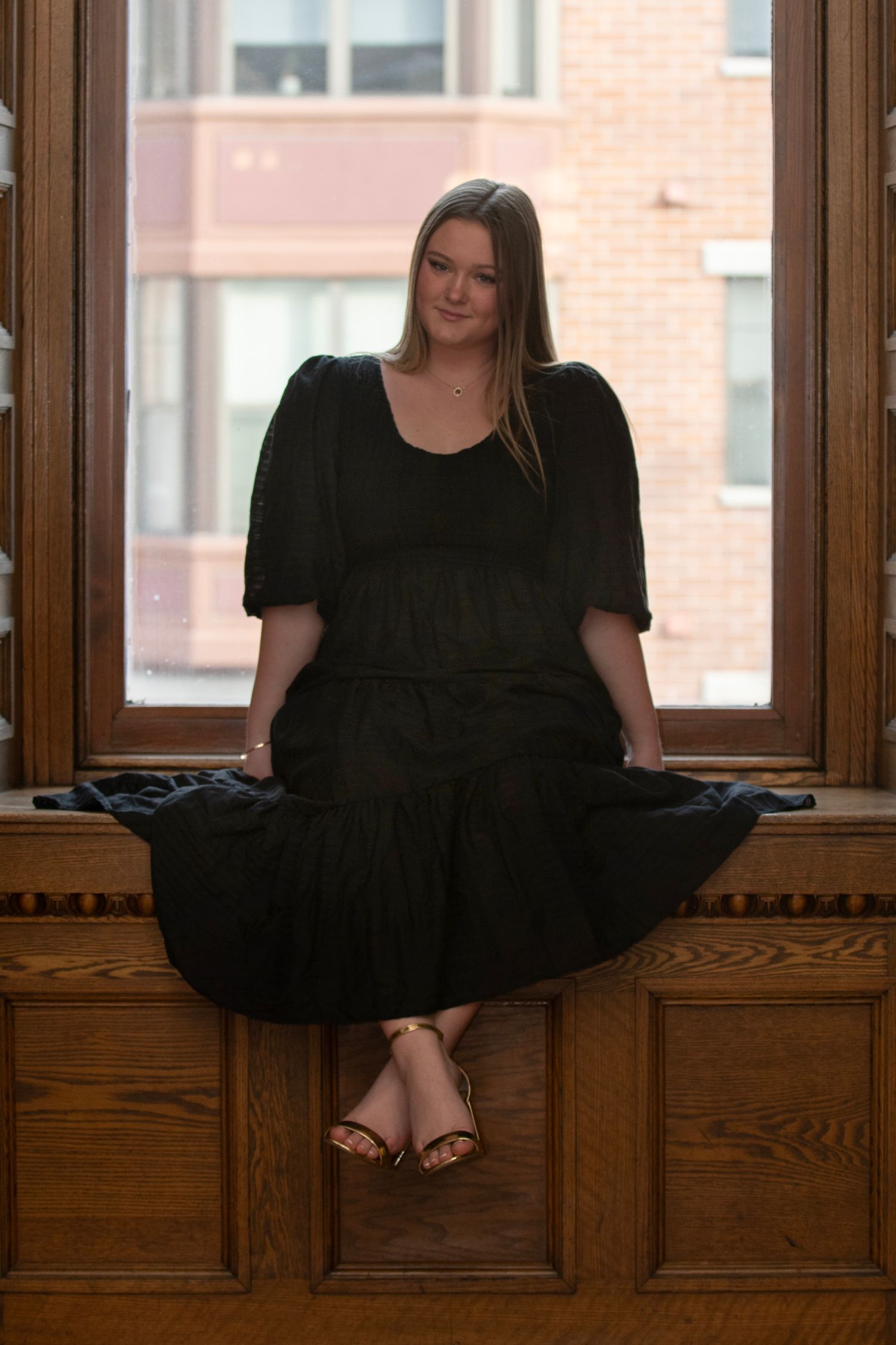 A woman in a black dress sits in a vintage wooden window alcove in a series of progressive poses.