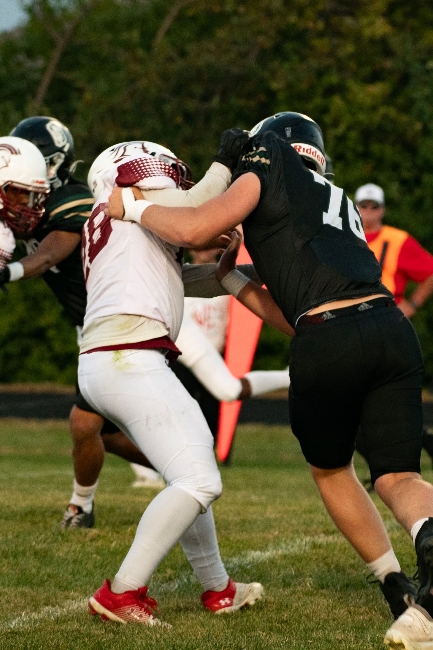 Football players in white and black uniforms bend at scrimmage line during a competitive match on grass field.
