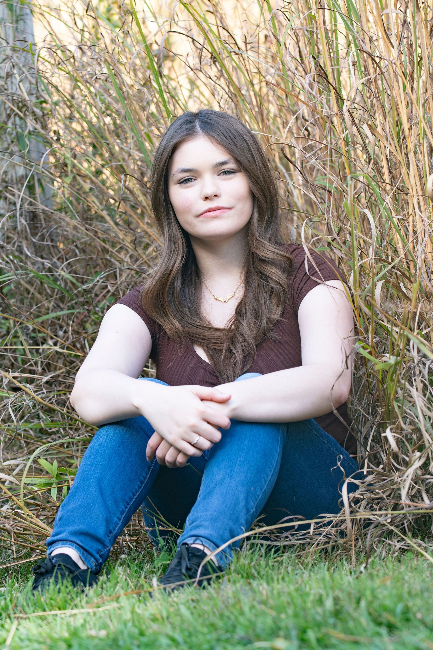 A relaxed high school senior posing on grass with tall dried plants creating a natural outdoor backdrop with Simply Junique portraits.