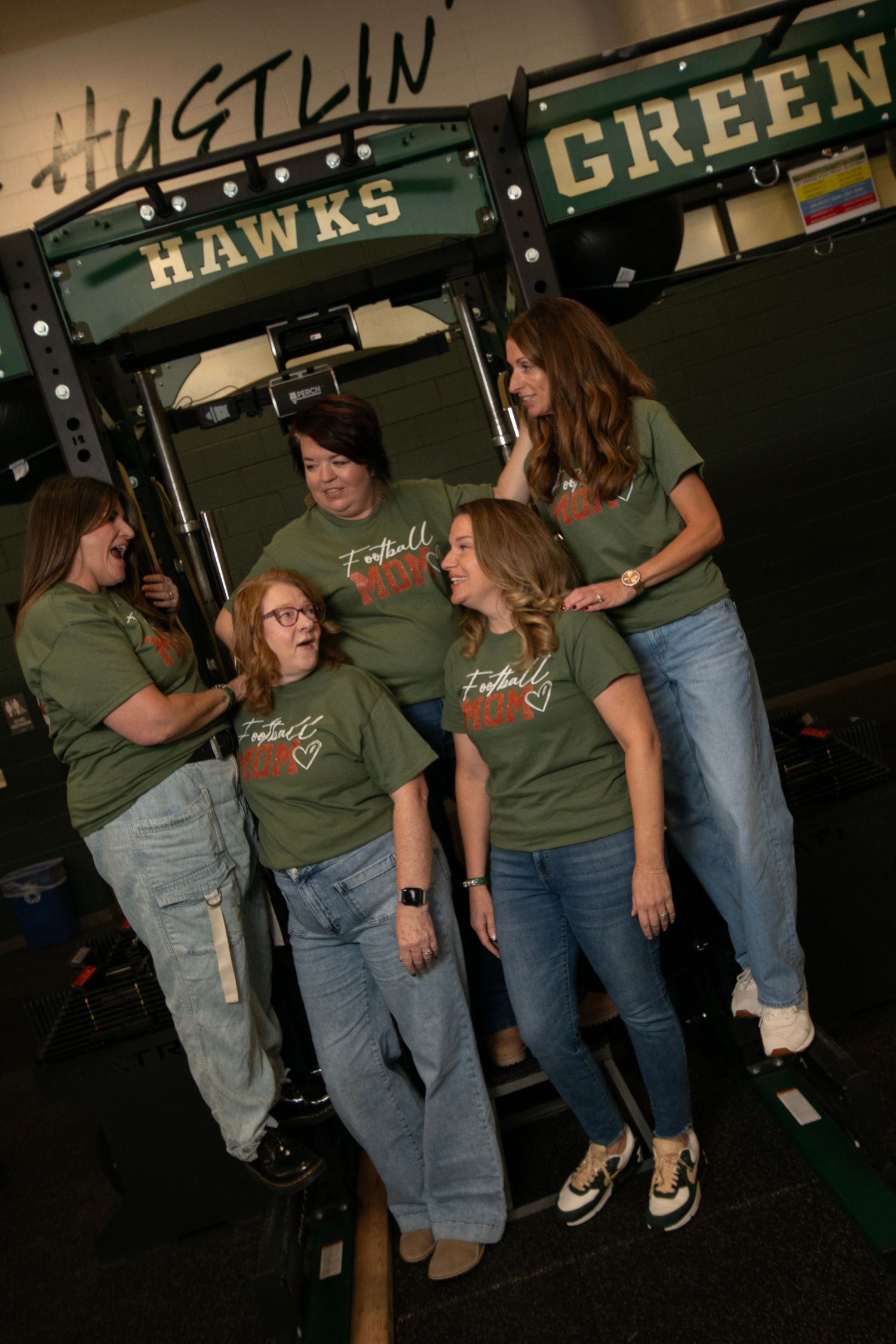 A group wearing matching green t-shirts and jeans stand together in a casual indoor setting.