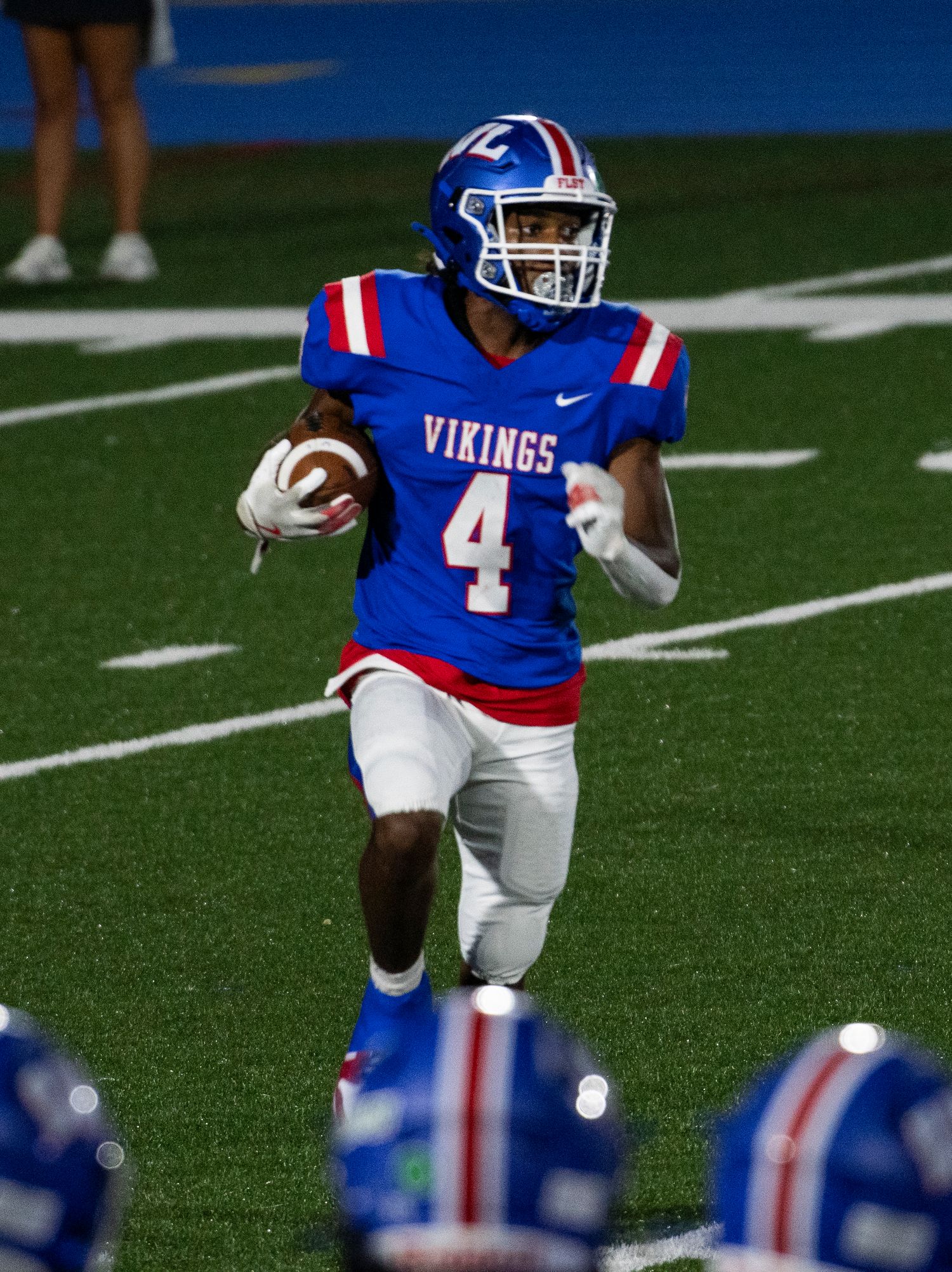 Vikings #4 football player in blue uniform runs with the ball during a high school night game.