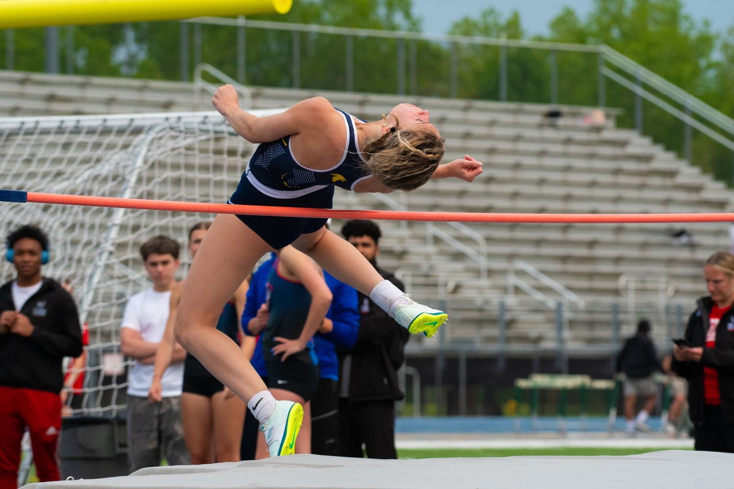Track athlete clears high bar during pole vault competition at outdoor stadium event.