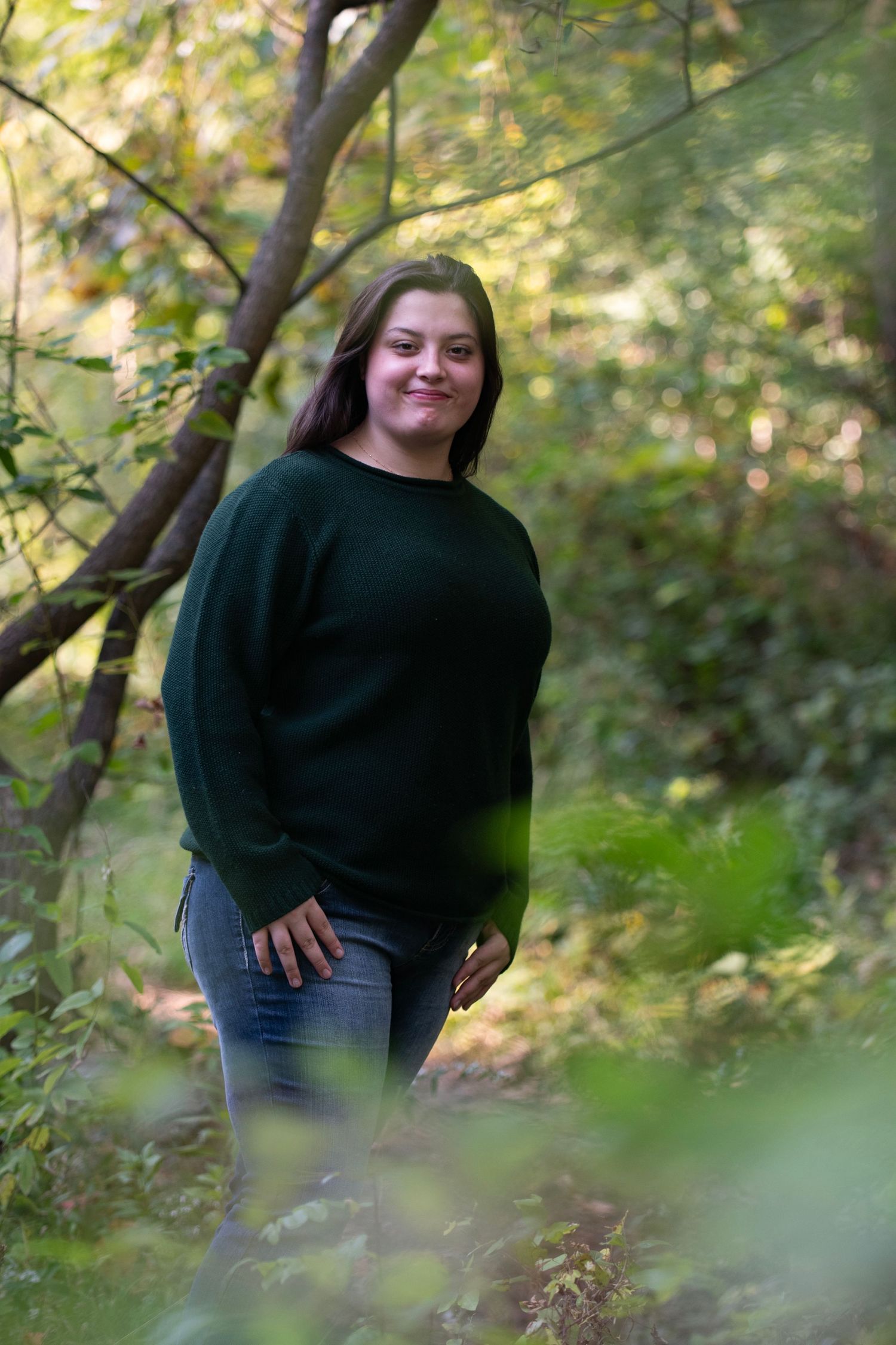 A person in a black sweater poses outdoors against a blurred green forest background in a photo series.