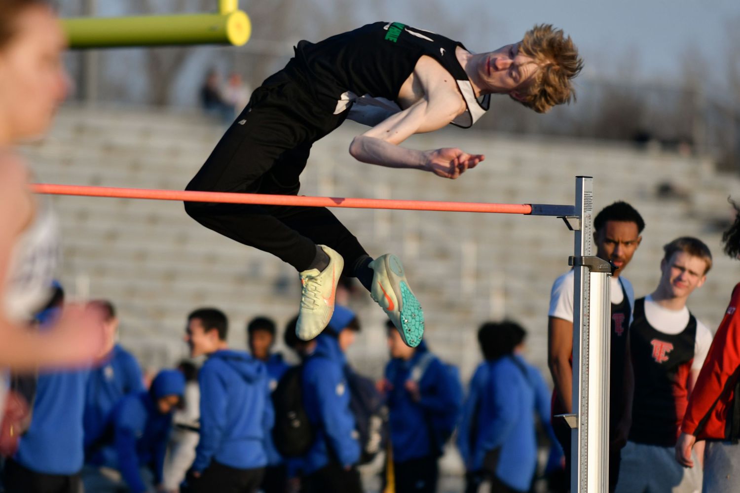Athlete performing high jump at a track and field meet, leaping over the bar in a black uniform.