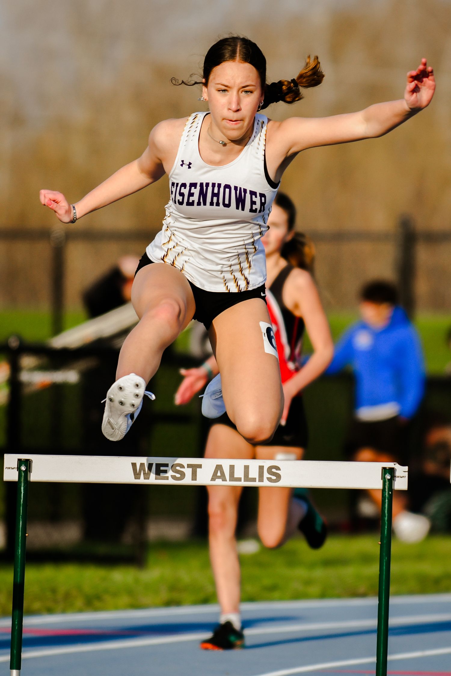 Athletes leaping over hurdles during a track competition at West Allis.