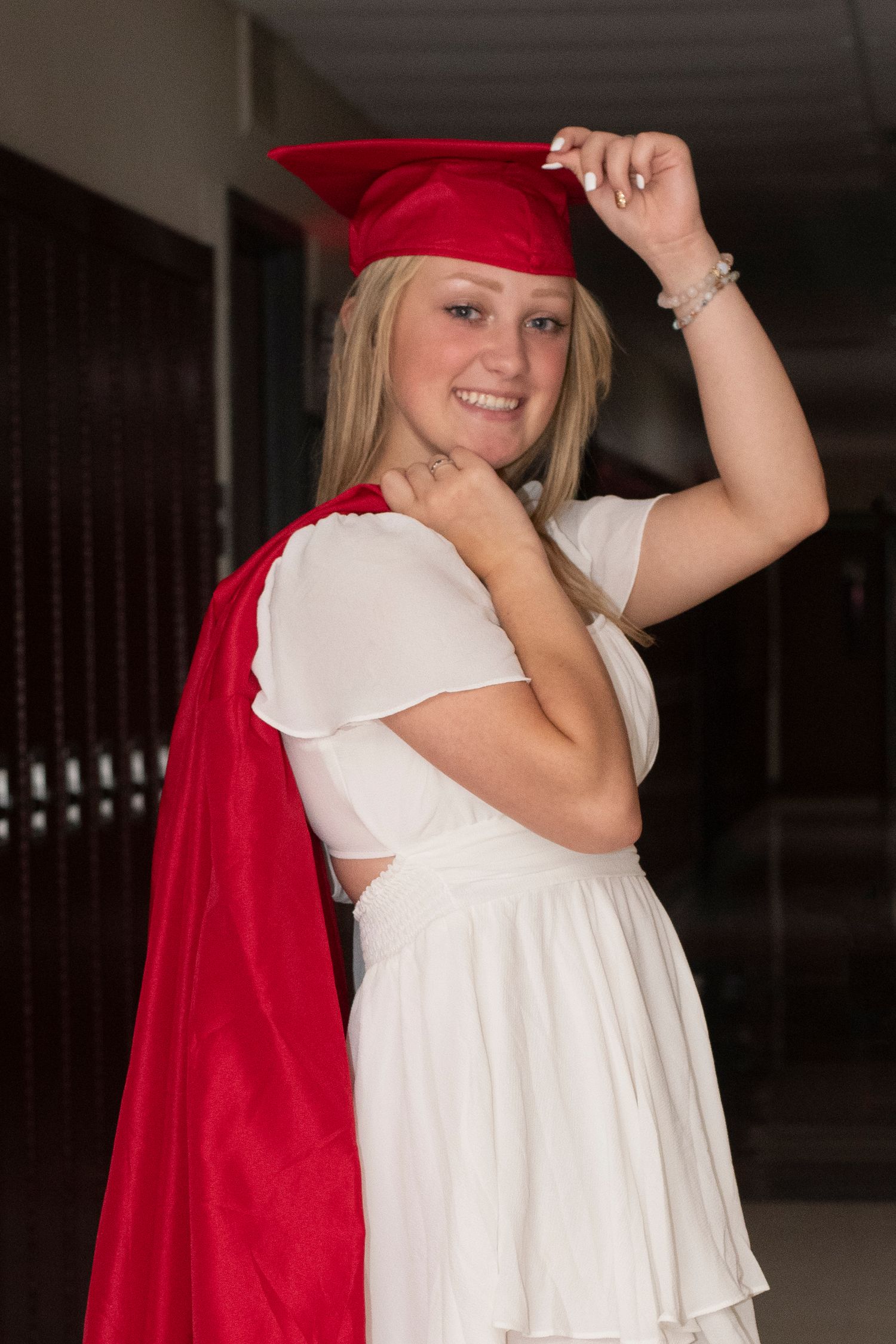 Figure in white dress and red cape poses playfully in indoor hallway setting.