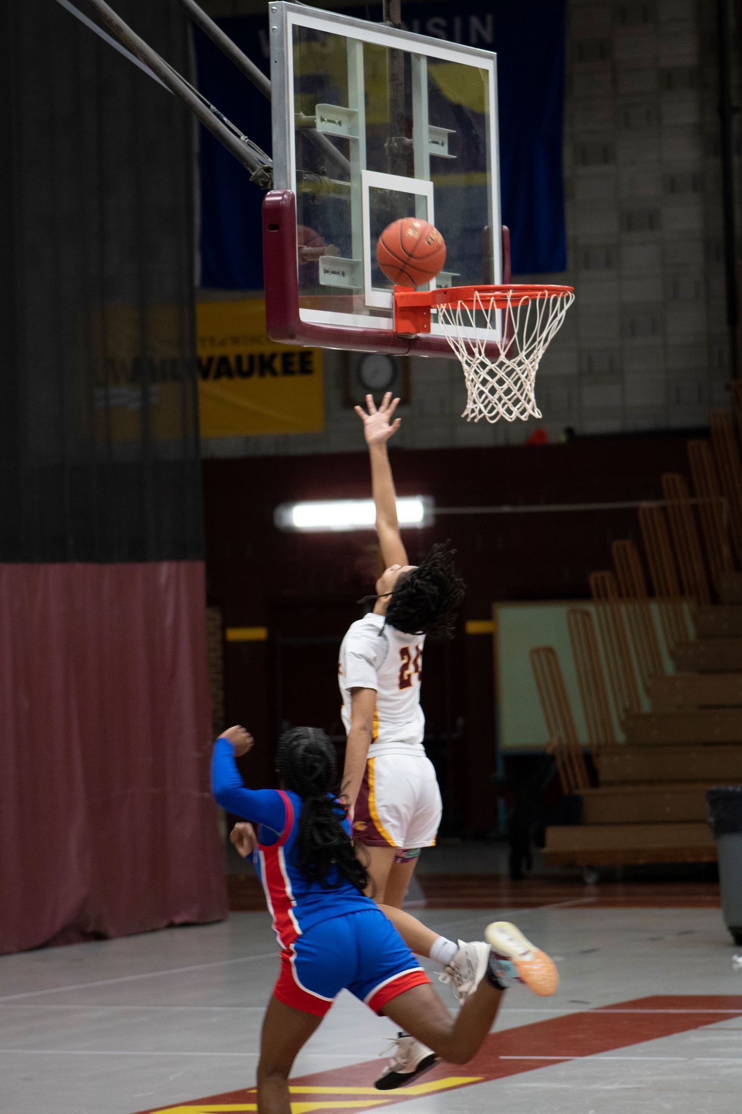 Two female basketball players compete near the hoop during an indoor game in Milwaukee, one attempting a layup shot.