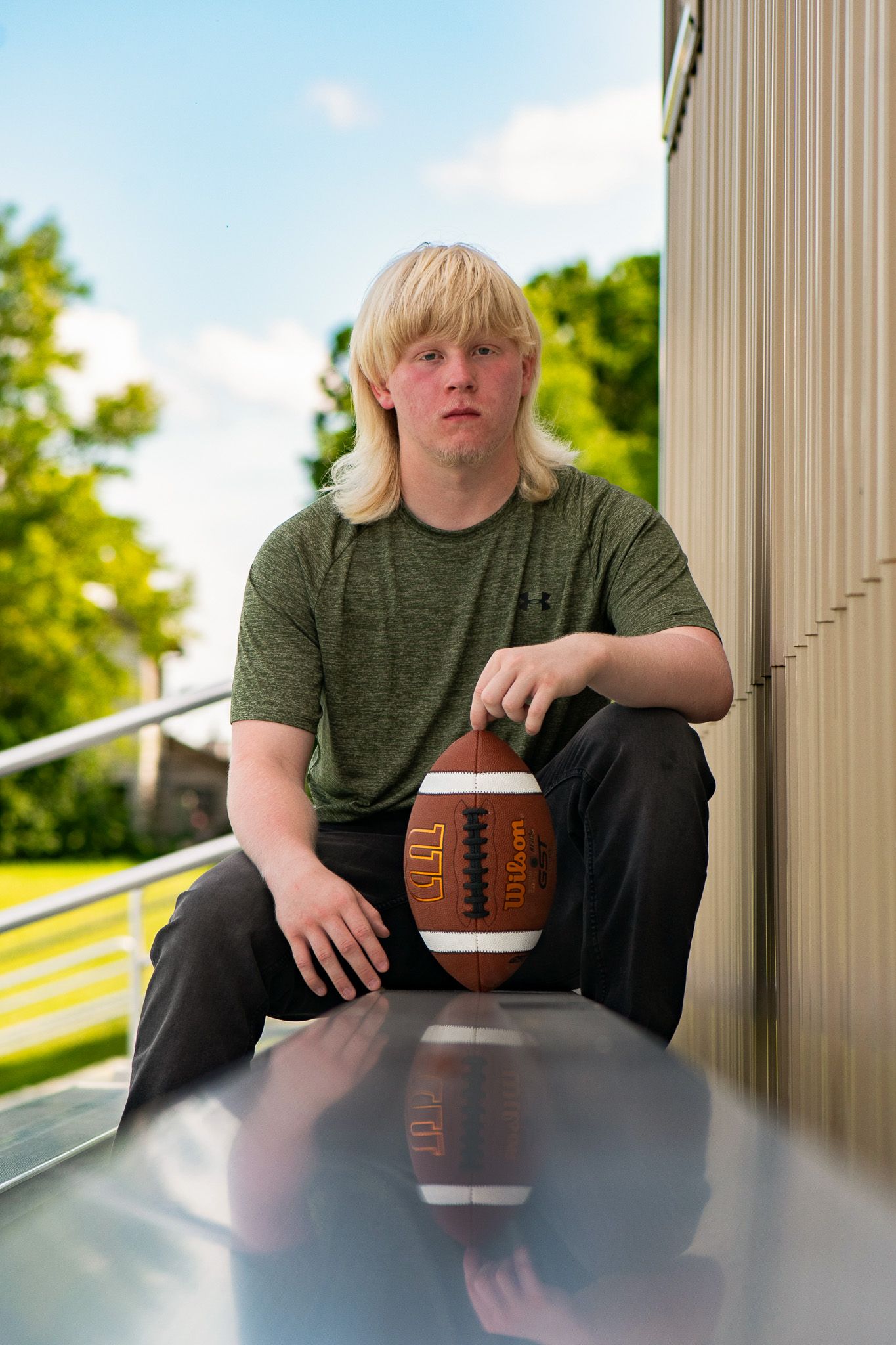 Person with football sitting at reflective table outdoors with columns in background. Game Day to Grad Day Senior Portrait Experience