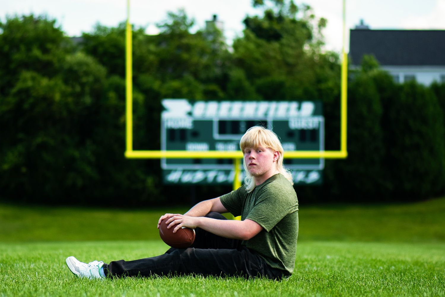 A person reclines on a football field with goal posts visible in the background. Game Day to Grad Day Senior Portrait Experience